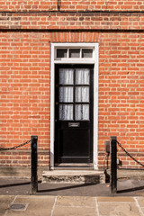 Victorian black external wooden door with glass panels on a red brick wall