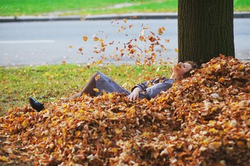a Young girl throwing autumn leaves in the air, lying on the ground in a big pile of fallen leaves.