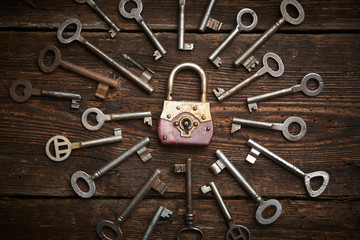 Vintage rusty padlock surrounded by old keys on a weathered steel background
