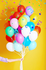 Woman holding many colorful balloons on yellow background