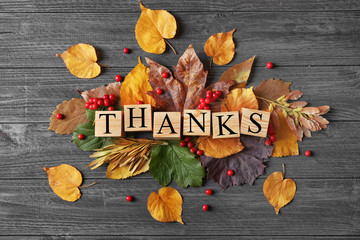 Autumn composition of leaves, berries and cubes with word THANKS on wooden background. Thanksgiving...