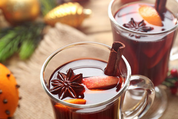 Glass cup of delicious mulled wine with Christmas decor on sackcloth, closeup