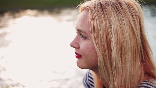 Young girl sitting on the gren grass near the river at sunset