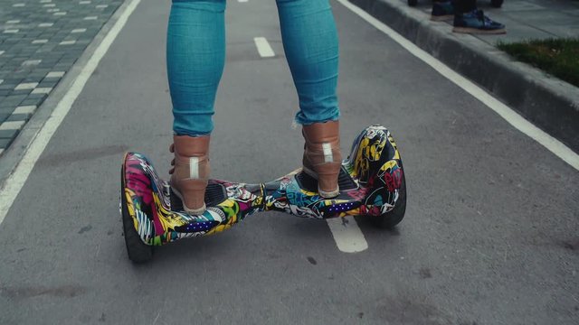 Close-up of female legs on a bright and colorful gyroscooter. Woman in jeans goes straight on paved track. Bike Lane. An alternative form of transport for young people.