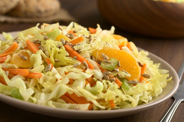 Fresh salad made of savoy cabbage, carrot, celery, and orange with roasted sunflower seeds on top, photographed with natural light (Selective Focus, Focus one third into the salad)