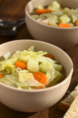 Savoy cabbage, carrot and potato stew or thick soup in bowls with slices of bread on the side, photographed on dark wood with natural light (Selective Focus, Focus in the middle of the first dish)
