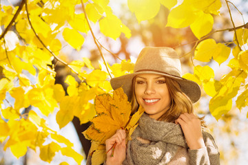 Modern beautiful young woman in autumn in park holding leaves