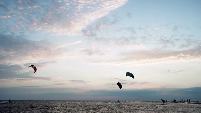 Kitesurfing. Silhouettes of four surfers riding on boards on the surface of waves and jumping with kite at sunset. Azov sea. HD