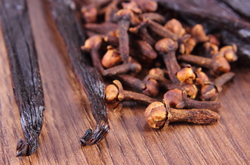 Closeup of cloves and fragrant vanilla on wooden surface plank