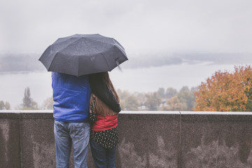 Romantic couple hugging in the street standing under an umbrella