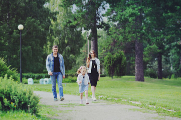 Family - mother, father and daughter walking in the Park full length.