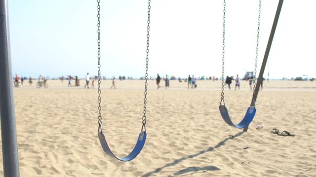 Venice Beach swings swinging empty, people walking along the beach in far background, summer day in Los Angeles