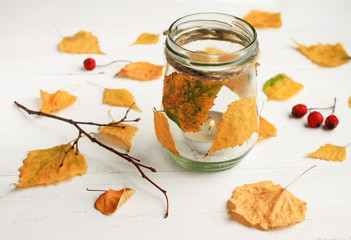Autumn-themed DIY candle. Tealight candle in glass jar, decorated dried golden leaves. Fall time...