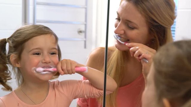 Young attractive mom and her cute daughter have fun brushing my teeth in the bathroom. Slow motion.
