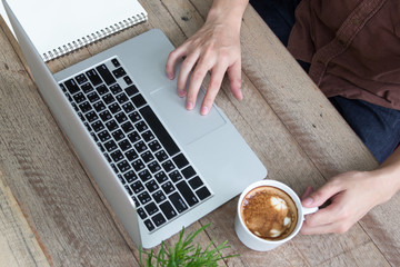 a man using laptop and coffee cup notepad on wood table