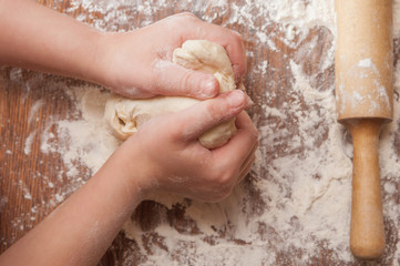 Making pie: kid's hands kneading the dough, rolling-pin and wheat flour on wooden table