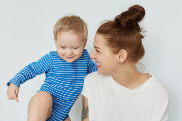 Funny portrait of toddler and happy young mother with bunch of brown hair looking at her tomboy....