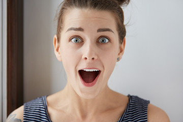 Close-up portrait of surprised Caucasian female in striped sleeveless T-shirt with blue eyes and...