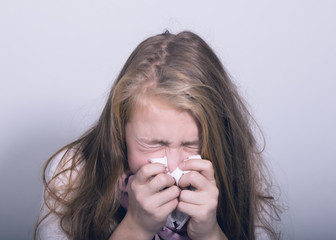 Sick young girl blowing her nose with paper tissue