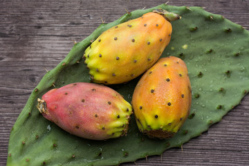 Fresh ripe whole prickly pears a leaf of the plant on wooden vin