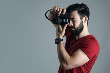 Profile view of young man taking photo with digital single lens camera. Moody desaturated portrait...