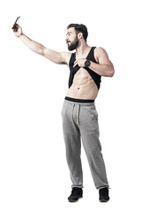 Muscular fit man showing abs muscles while taking selfie with smart phone. Full body length portrait isolated over white studio background
