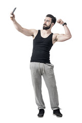 Fototapeta na wymiar Fit young man flexing bicep arm muscle while taking selfie photo with mobile phone. Full body length portrait isolated over white studio background