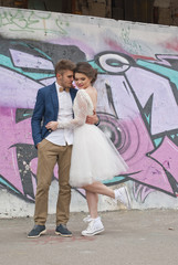 Just married loving hipster couple in wedding dress and suit outdoor in city setting against colorful graffiti wall. Happy bride and groom walking running and dancing. Romantic Married young family. 