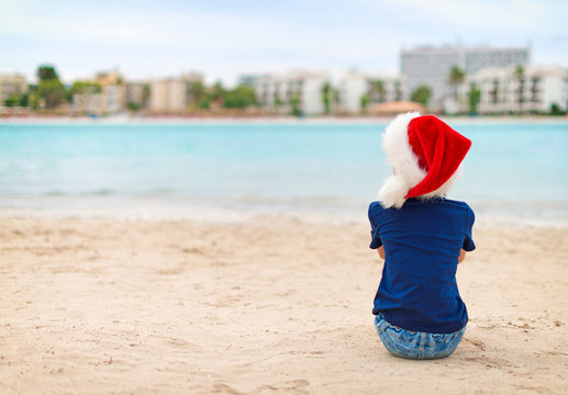 Funny little girl sitting on the beach. Christmas and new year vacations concept.