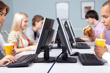 Five students sitting at computers and having snack
