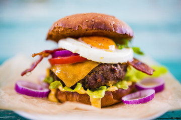 Tasty grilled beef burger in crispy shortbread with fried egg and bacon served on a rustic wooden table. Street food.