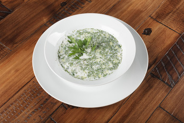 Russian and ukrainian traditional cold soup (okroshka) in a white plate. Wooden background