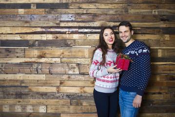 Obraz na płótnie Canvas Young couple near wooden wall celebrating Christmas