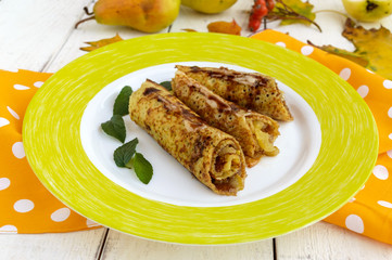 Fragrant sweet pancakes with caramelized pears and chocolate syrup and mint leaves on a white background.