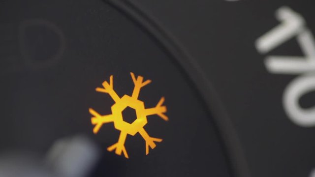 Color close up footage of a car's snow warning symbol lighting up on the dashboard.