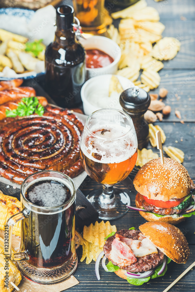 Wall mural Beer and snack set. Octoberfest food frame concept. Variety of beers, grilled sausages, burgers, fried potato, corn, chips and sauces on dark wooden scorched background. Selective focus