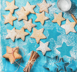 Fototapeta na wymiar Christmas or New Year holiday food background. Sweet gingerbread cookies in shape of star sprinkled with sugar powder, cinnamon sticks and metal shapes on blue painted plywood background, top view