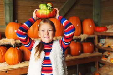 Fototapeta na wymiar Adorable little girl of 8-9 year old choosing halloween pumpkin on farm market, having fun with unusual different kind of pumpkins