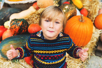 Adorable little boy of 5-6 year old with big thumbs up choosing halloween pumpkin on farm market
