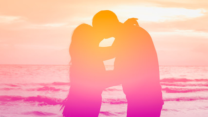 Silhouette couple kissing in pink tone on the beach with heart bokeh for valentines theme.