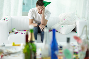 Crapulent man sitting on sofa in room after a cheerful party