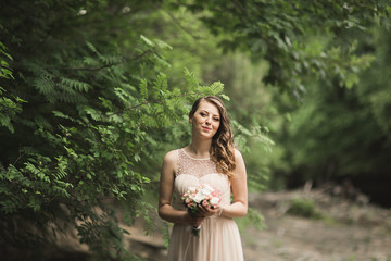 Beautiful luxury young bride inwedding dress standing near river with mountains on background