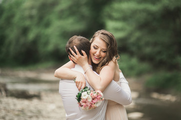 Elegant gentle stylish groom and bride near river with stones. Wedding couple in love