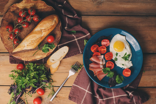 fried eggs with tomato, basil and prosciutto, table set for cozy breakfast at home