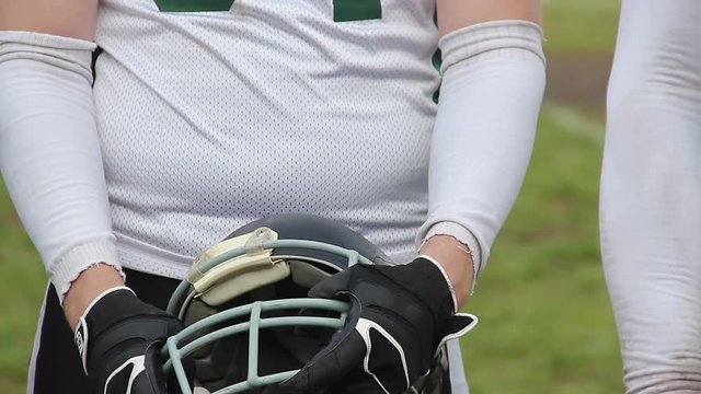 Disciplined football player holding helmet in hands, team preparing for match
