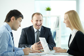 Three business people laughing while communicating at meeting