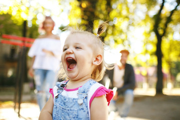 Cute child in jeans jumpers screams while parents stand on the b