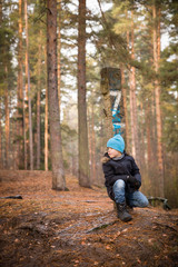 Cute kid boy sitting on the ground in the forest on a cold autumn day. Child walking outdoors.