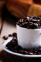 Grains of roasted coffee in a white cup, vintage wooden backgrou