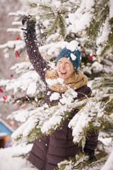 Portrait of happy smiling young woman having fun and playing with snow under Christmas tree. Girl walking in the winter park. Christmas and winter concept.